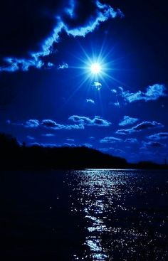 the sun is shining brightly in the dark sky over the water at night with clouds and blue hues