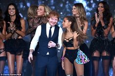 a man in a tuxedo standing next to two women on stage with other dancers behind him