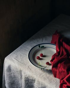 a plate with some cherries on it sitting on a table next to a red cloth