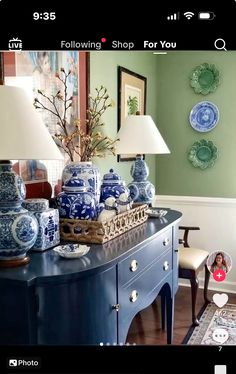 a blue and white table with vases on it in a room that has green walls