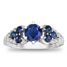 Take her breath away with this colorful vintage-inspired sapphire and diamond engagement ring. Expertly crafted in 14K white gold, the eye is drawn to the 6.0mm bright blue sapphire center stone. Trios of smaller blue sapphires flank each side of the center stone, while shimmering diamonds and intricate milgrain detailing adorn the ring's split shank. An elegant choice, designed to sparkle for a lifetime, this ring captivates with 1/8 ct. t.w. of diamonds and a polished shine. Heirloom Blue Diamond Ring In 14k White Gold, Vintage Blue Sapphire Ring With Halo Setting, Heirloom Blue Diamond Ring With Accents, Heirloom Blue Sapphire Ring With Diamond Accents, Classic Blue Sapphire Ring In 14k White Gold, Vintage Blue Sapphire Ring With Diamond Accents, Vintage Blue Sapphire Ring In Platinum, Heirloom Blue Sapphire Diamond Ring, Classic Blue Diamond Ring In 14k White Gold