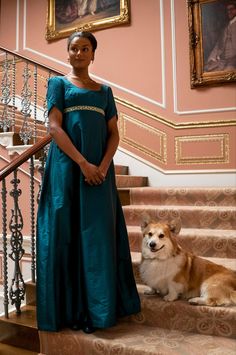 a woman in a green dress standing on stairs with a dog sitting next to her