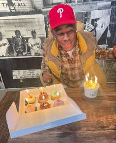 a young man sitting at a table with some cupcakes in front of him