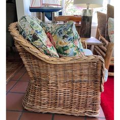 a wicker chair with two pillows on it in front of a lamp and window