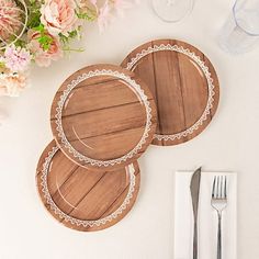 three wooden plates and two silverware on a white table with flowers in the background