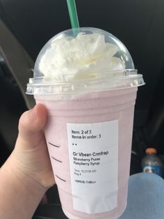 a hand holding up a pink drink with whipped cream on top