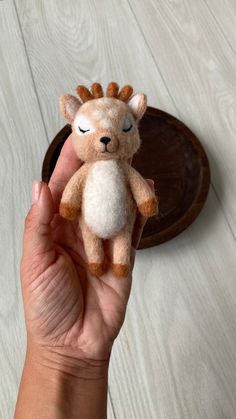 a hand holding a small stuffed animal in front of a wooden tray on the floor