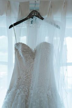 two wedding gowns are hanging on a rack in front of a window with sheer curtains