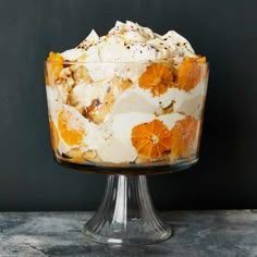 an orange trifle with whipped cream and fruit toppings on a glass pedestal in front of a blackboard