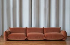 an orange couch sitting on top of a hard wood floor next to a white curtain