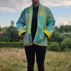 a woman standing in a field with her hands on her hips wearing a blue and yellow jacket