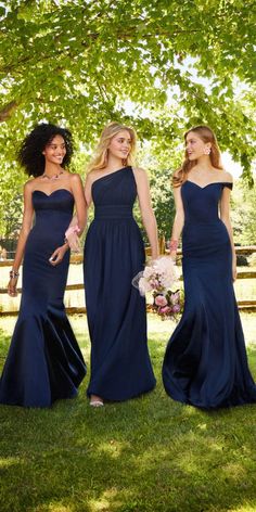 three bridesmaids in blue dresses standing under the shade of a tree and holding bouquets