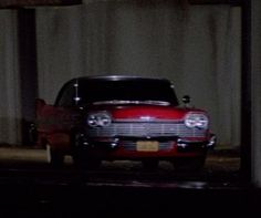 an old red car parked in a parking garage at night time with the lights on