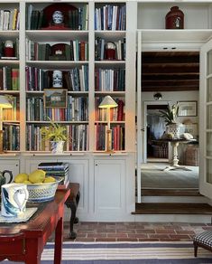 a room filled with lots of books on top of white bookcases next to a red table