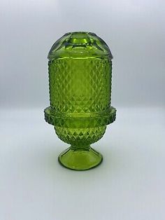 a green glass vase sitting on top of a white tableclothed surface with an open lid