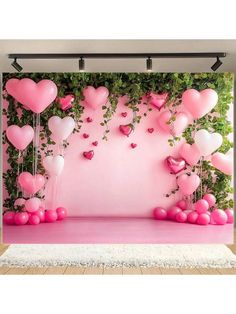 pink and white balloons are floating in the air on a stage with greenery behind it