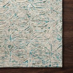 a white rug with blue and green designs on the floor in front of a wooden wall