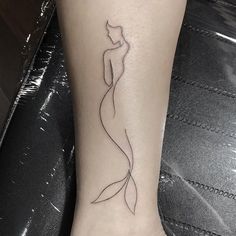 a woman's foot with a tattoo on it that has a line drawing of a mermaid