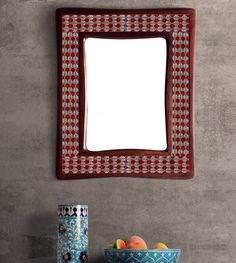 a mirror sitting on top of a wall next to a bowl of fruit and a vase