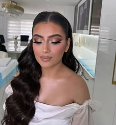 a woman with long dark hair wearing a white dress and makeup looks at the camera