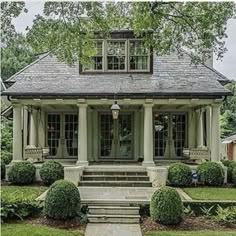 a house that is in the middle of some grass and trees with bushes around it