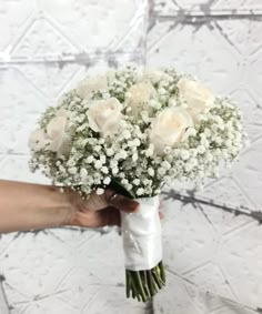 a bouquet of white roses is held by someone's hand in front of a wall