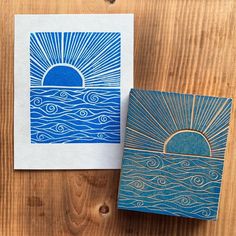 two blue and white greeting cards with the sun rising over water on top of them