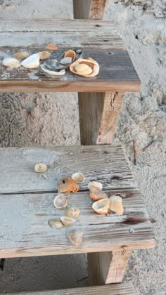 two wooden benches sitting on top of a sandy beach next to the ocean with seashells on them