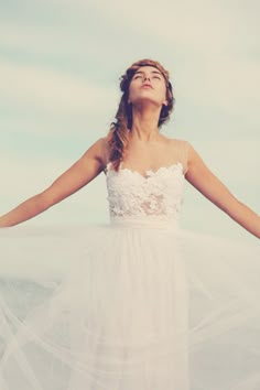 a woman in a white dress with her arms spread out to the side, looking up into the sky