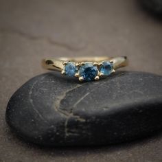 This delicate yet bold three-stone ring design has a subtle curve in the setting and works incredibly well as a wedding band, engagement ring, or stand-alone statement ring. This version is made in 14 karat yellow gold and features three stunning teal blue Montana Sapphires mined in the US. These brilliant sapphires have a cool smoky teal blue color palette that contrasts beautifully with the warm yellow gold setting. Sapphires are very durable stones for everyday wear. Sapphire is the birthston 3 Stone Sapphire Ring, 14k Gold Three-stone Diamond Ring For Anniversary, 14k Gold Three Stone Diamond Ring For Anniversary, Anniversary 14k Gold Three-stone Diamond Ring, Timeless Gold Three-stone Sapphire Ring, Yellow Gold Three Stone Topaz Ring Fine Jewelry, Timeless Three Stone Ring In 14k Gold, Yellow Gold Sapphire Ring With Tension Setting For Wedding, Yellow Gold Three Stone Diamond Promise Ring