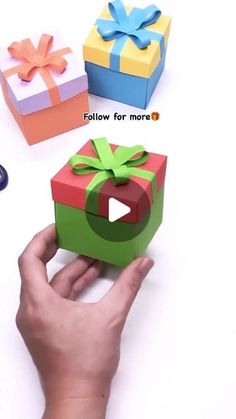 someone is holding an origami gift box with a bow on it and another present in the background