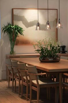 a dining room table and chairs with plants in the center on top of it, along with hanging lights