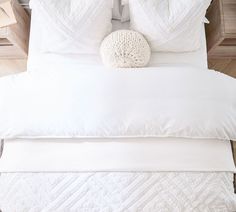 a white bed topped with pillows next to a wooden headboard and night stand on top of a hard wood floor