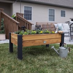 a wooden planter with flowers in it sitting on the grass next to a house