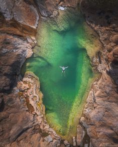 an aerial view of a body of water surrounded by rocks and cliffs with a bird flying over it