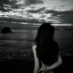 a woman sitting on the beach looking out at the ocean