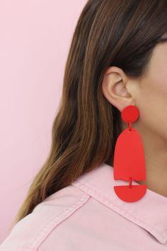 a woman wearing large red earrings with an oval shaped design on the back of her ear