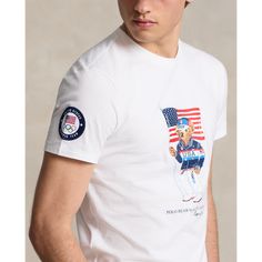 Part of the Polo Ralph Lauren Team USA Collection this Custom Slim Fit T-shirt features our iconic Polo Bear sporting the uniform Ralph Lauren designed for Team USA's flagbearer to wear during the Closing Ceremony of the Olympic and Paralympic Games Paris 2024. Ralph Lauren White T-shirt With Graphic Print, Ralph Lauren Cotton Tops With Letter Print, Casual Ralph Lauren Tops With Letter Print, Ralph Lauren Casual Tops With Letter Print, Cotton Sports T-shirt With Flag Print, Ralph Lauren Crew Neck Tops With Letter Print, Sporty Ralph Lauren Tops With Graphic Print, Sporty Ralph Lauren Graphic Print Tops, Sporty Ralph Lauren Top With Graphic Print