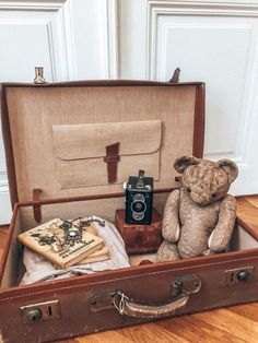 a teddy bear sitting in an open suitcase on the floor next to books and other items