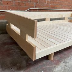 a wooden bed frame sitting on top of a cement floor next to a brick wall