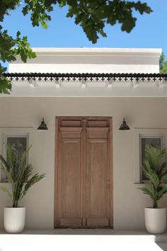 two potted plants sit in front of a white building with wooden doors and windows