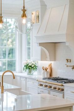 a kitchen with white cabinets and marble counter tops, gold faucet lights over the stove