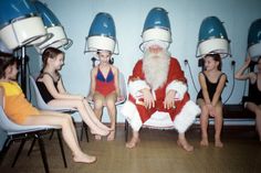 a group of children sitting around santa clause in front of some hair dryers on their heads