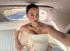 a woman sitting in the back seat of a car wearing a white dress and holding her arm out