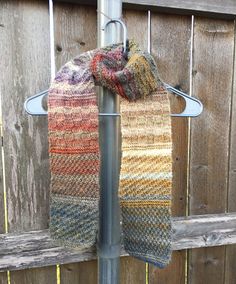 two scarves are hanging on a metal pole next to a wooden fence and wood planks