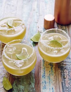 two margaritas with lime and salt garnish sit next to each other on a wooden table