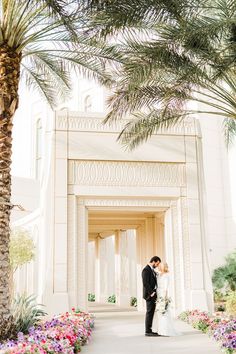 a bride and groom standing in front of a building with palm trees on either side