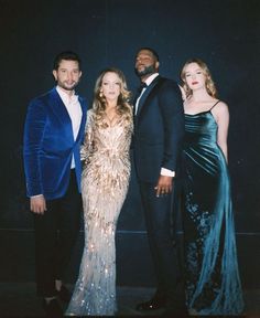 three people standing next to each other in front of a dark background wearing evening gowns