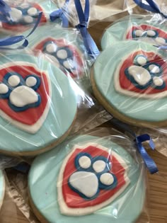 decorated cookies in the shape of dogs paw prints on plastic wrappers with blue ribbons