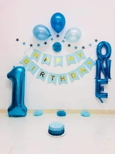 a blue birthday cake and balloons in the shape of an number one on a table